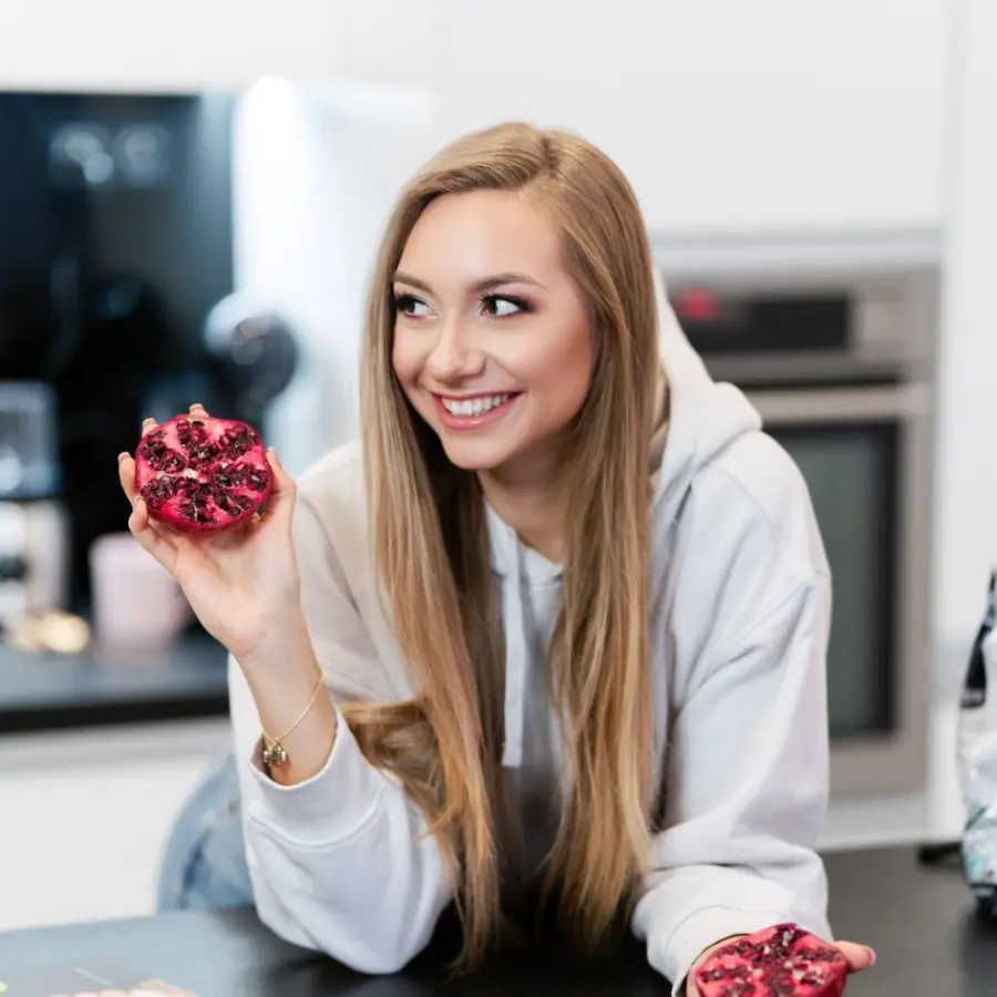 Marta Czmielnik uśmiecha się w kuchni trzymając przekrojony owoc granatu.